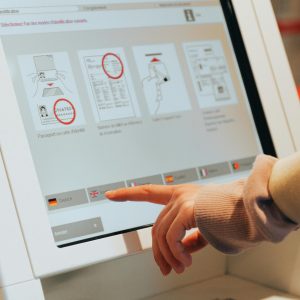 Hand interacting with airport self-service kiosk for check-in.